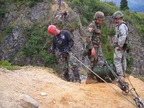 2003 Jeep TJ - Soldiers practice rappelling techniques on a steep, rocky incline with trees in the background.