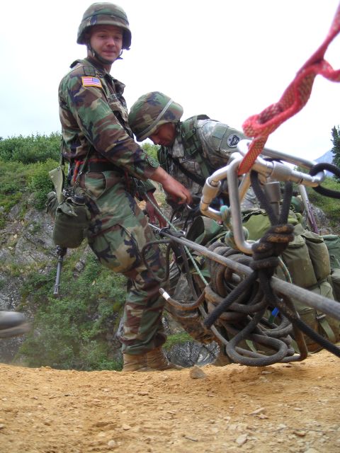 2003 Jeep TJ - Two soldiers in camouflage uniforms are seen working with ropes and carabiners, preparing equipment for an operation on a terrain.