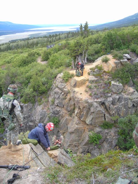 2003 Jeep TJ - Military personnel are engaged in a training exercise on a steep, rocky incline overlooking a wide valley.