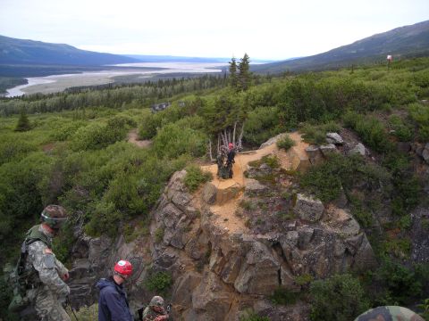 2003 Jeep TJ - A group of people in tactical gear and helmets are rappelling down a rocky cliff face, with a wide valley and mountains visible in the dist…