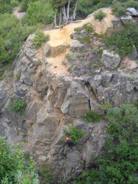 2003 Jeep TJ - A person is rock climbing on a large, textured cliff face with trees and bushes around.