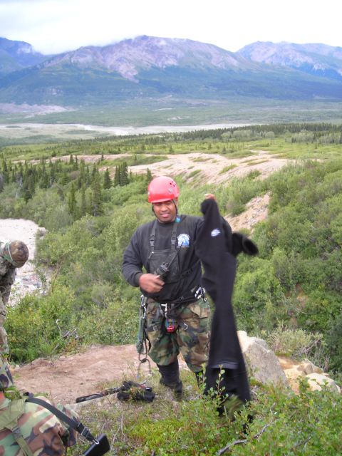 2003 Jeep TJ - A man holds a black garment while standing on a hill with mountains in the distance.