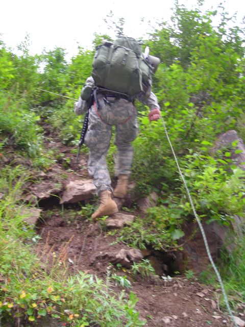 2003 Jeep TJ - A soldier ascends a steep, vegetated slope, using a rope for assistance.