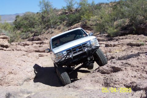 1993 Ford Bronco - This SUV is navigating a rocky trail with steep inclines and clear blue skies.