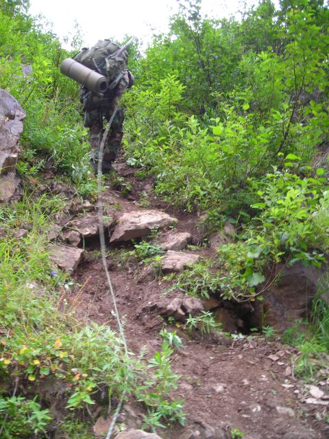 2003 Jeep TJ - A person ascends a steep, overgrown trail, using a rope for assistance.
