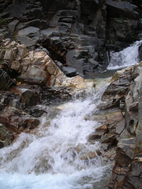 2003 Jeep TJ - A rushing waterfall flows down a rocky mountainside, surrounded by dark and light-colored stone formations.