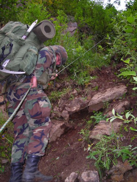 2003 Jeep TJ - Two soldiers ascend a steep, rocky incline, using ropes for support and carrying heavy packs.
