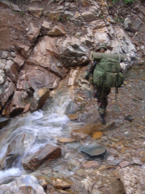 2003 Jeep TJ - A person wearing camouflage and a large backpack navigates a rocky stream bed.