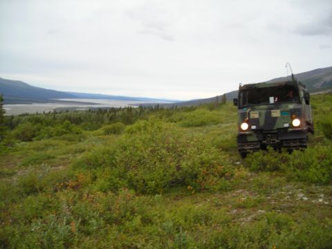 2003 Jeep TJ - An all-terrain vehicle with tracks navigates a green, open terrain under a cloudy sky.