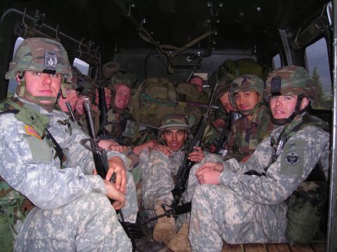 2003 Jeep TJ - Soldiers are packed into the back of a military vehicle, armed and ready.