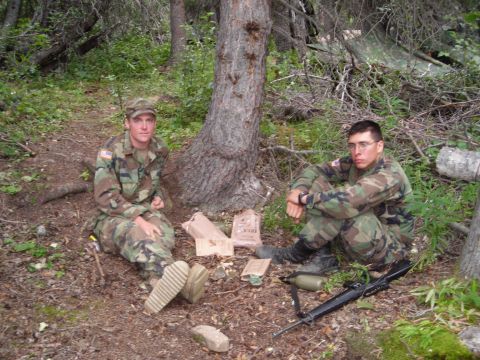 2003 Jeep TJ - Two soldiers take a break in a wooded area, surrounded by trees and foliage, with their rations and equipment nearby.