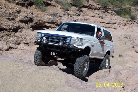1993 Ford Bronco - A white 1993 Ford Bronco navigates a challenging rocky trail, demonstrating its off-road capabilities.