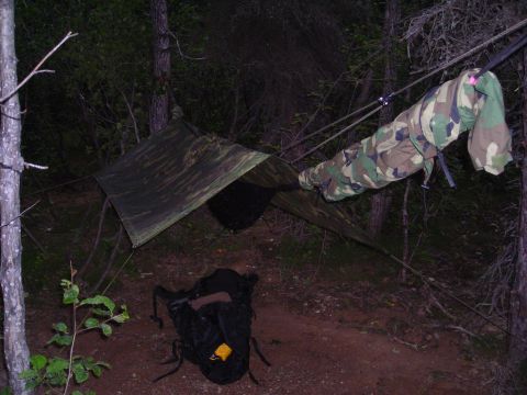 2003 Jeep TJ - A makeshift campsite is set up in a wooded area with a tarp shelter and camping gear.