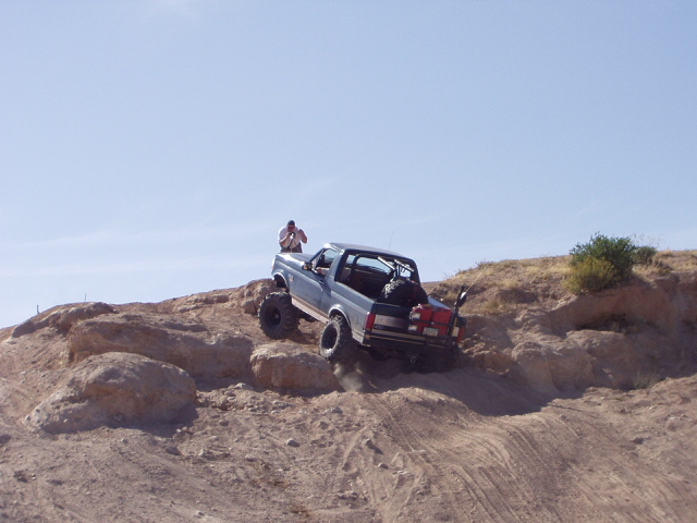 Open-top blue-gray 4x4 with roll bar cresting a steep rocky desert hill