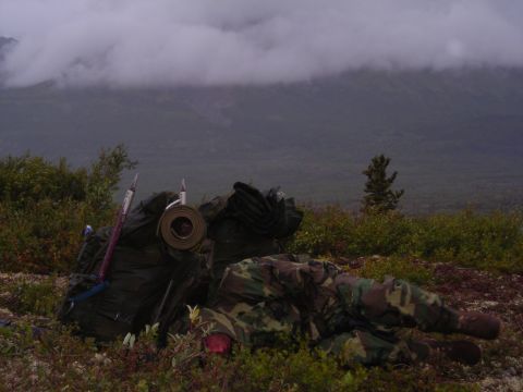 2003 Jeep TJ - A person in camouflage gear rests amongst camping equipment with a misty mountain landscape behind them.