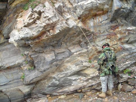 2003 Jeep TJ - A soldier prepares to descend a steep, layered rock formation using a rappelling rope.