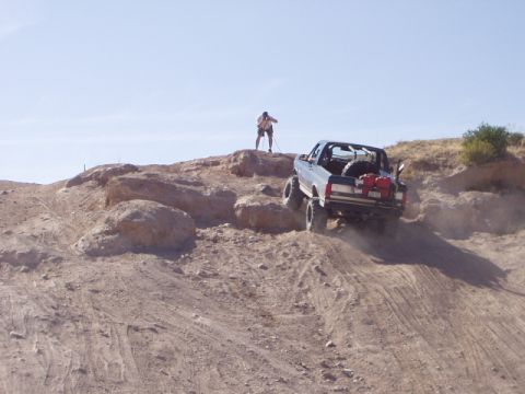 1993 Ford Bronco - A modified truck navigates a challenging off-road terrain under a clear blue sky.
