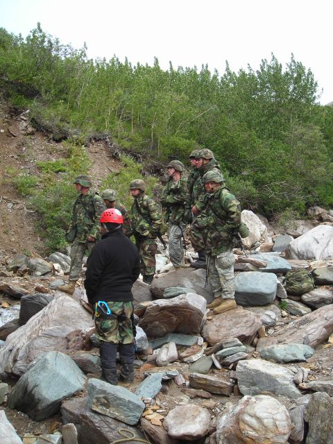2003 Jeep TJ - A group of soldiers in camouflage stand on a rocky slope surrounded by trees.