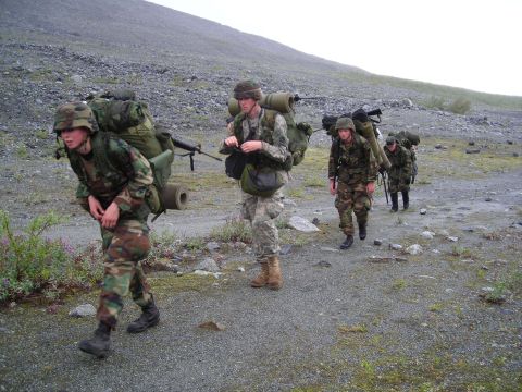2003 Jeep TJ - Soldiers carrying heavy packs traverse a desolate, rocky terrain under an overcast sky.