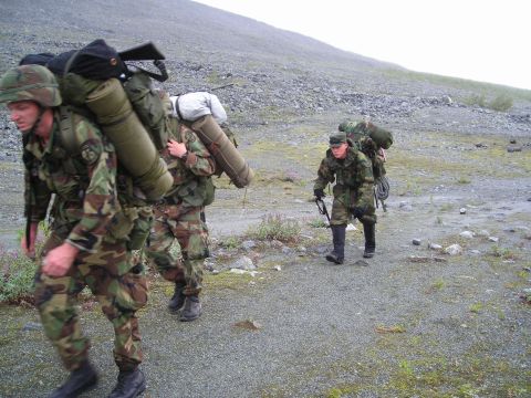 2003 Jeep TJ - Soldiers carrying heavy packs trek across a desolate, rocky landscape under an overcast sky.