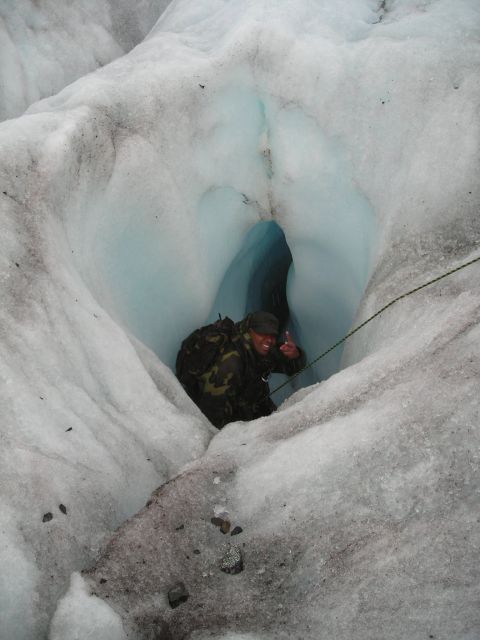 Person in camouflage clothing gives a thumbs up inside a blue ice cave