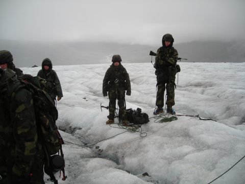 Soldiers in camouflage gear stand on a glacier with ice axes and ropes