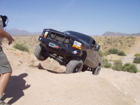 1993 Ford Bronco - A modified truck navigates a steep, sandy incline under a clear blue sky.