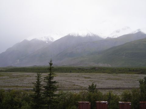 Snow-capped mountains under a hazy sky above a treeline and a rocky plain