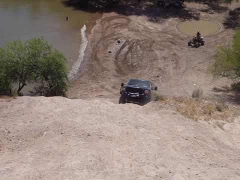 1993 Ford Bronco - A black Ford truck navigates a steep, sandy slope towards a shoreline with a person in the water.