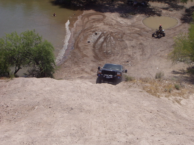 Black lifted SUV parked in a sandy desert wash beside a river, seen from above
