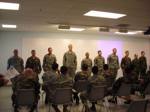 Military personnel standing and seated in a room with fluorescent lighting