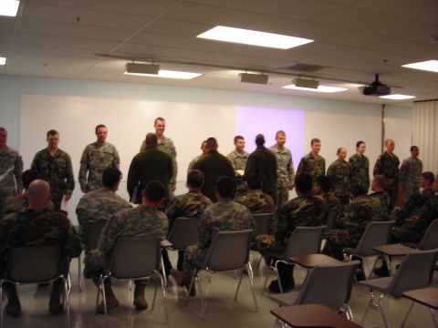 Military personnel standing and sitting in a classroom with a projector screen