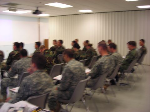 People in military uniforms sitting in chairs facing a screen in a classroom setting