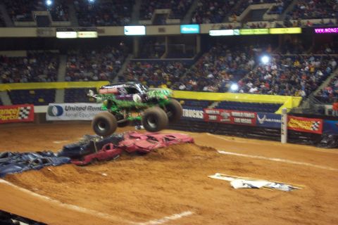 1987 Ford Bronco - A monster truck performs a jump over a pile of crushed cars during an event in an arena.
