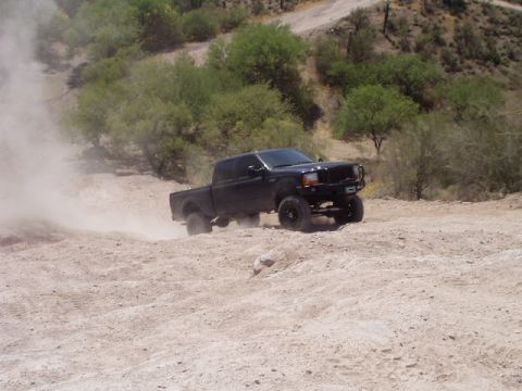 1993 Ford Bronco - Black Ford F-250 Super Duty pickup truck driving off-road on a dusty trail.