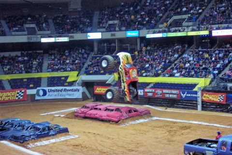 1987 Ford Bronco - Monster truck performs a jump over a row of crushed cars during an event.