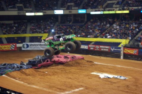 1987 Ford Bronco - A monster truck jumps over a pile of crushed cars during a competition.