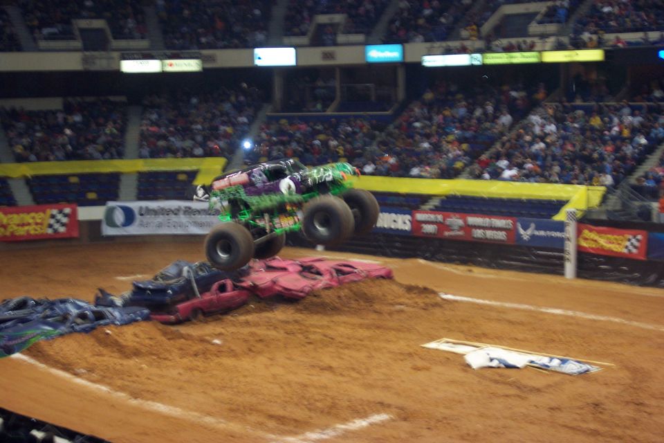 Green monster truck with purple accents airborne over crushed cars