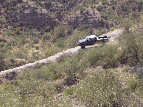 1993 Ford Bronco - A pickup truck navigates a rough, unpaved road through a dry, brush-covered landscape.