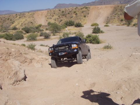 1993 Ford Bronco - A black pickup truck navigates a dusty, off-road trail with arid hills in the background.