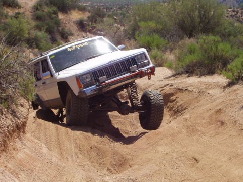 1993 Ford Bronco - A white Jeep Cherokee navigates a steep dirt trail, its off-road capabilities and a custom windshield decal.