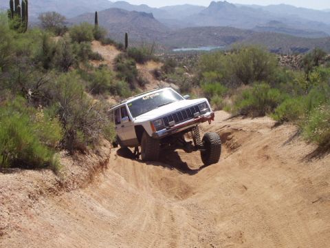 1993 Ford Bronco - Jeep Cherokee XJ navigates a challenging off-road trail with steep inclines and loose dirt.