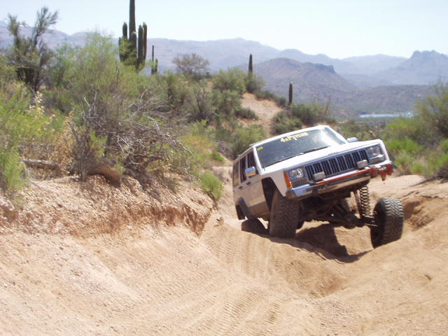 White Jeep Cherokee XJ climbing dirt bank on desert off-road trail
