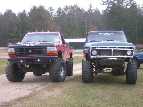 1977 Ford F-150 - Two lifted pickup trucks, one blue and one red, are parked side-by-side on a dirt road.