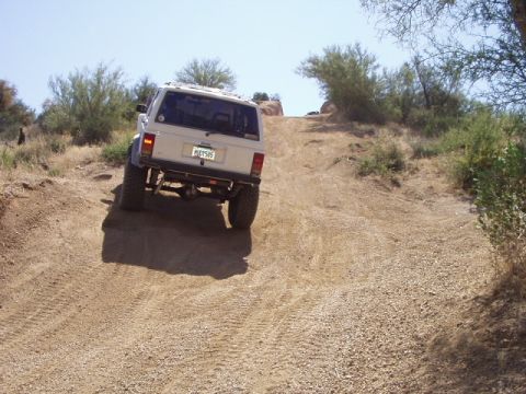 1993 Ford Bronco - A white SUV navigates a steep, dry dirt incline under a clear blue sky.