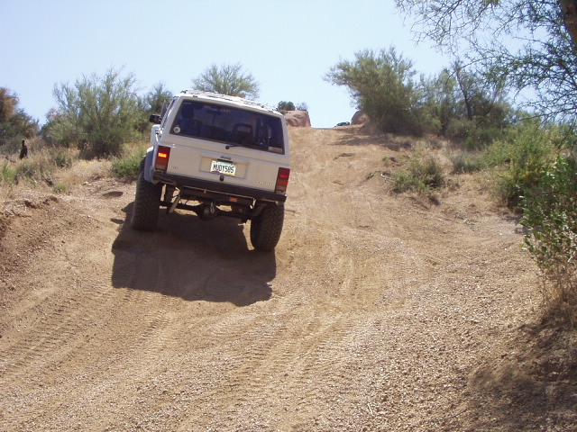 White lifted Jeep Cherokee XJ climbing a steep dirt hill, seen from behind