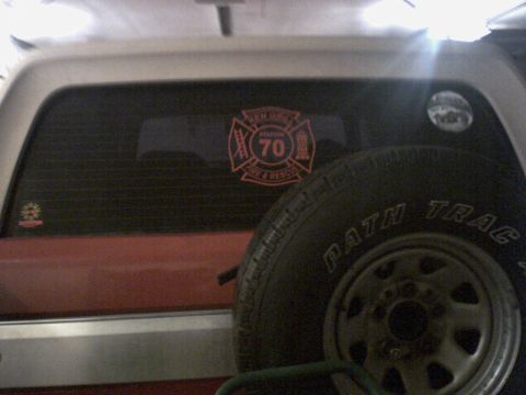 1989 Ford Bronco - A close-up view of a vehicle's rear window, a fire department emblem and a spare tire mounted nearby.