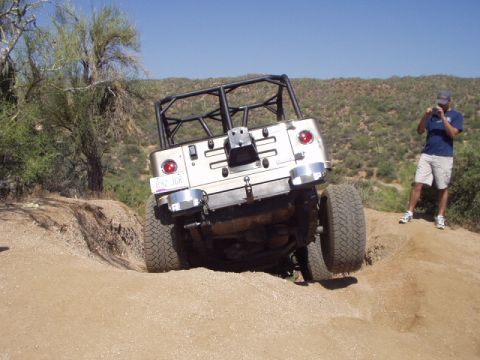 1993 Ford Bronco - Silver Jeep Wrangler TJ navigates a steep dirt trail with a person photographing the action.