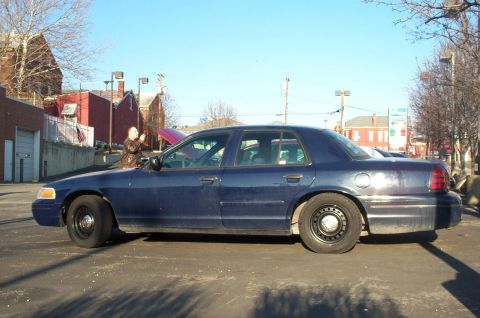 2001 Ford Crown Victoria - A dark blue 2001 Ford Crown Victoria sedan is parked with its hood open under a clear sky.