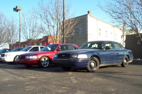 2001 Ford Crown Victoria - Multiple Ford Crown Victoria police cars are parked in a lot on a sunny day.